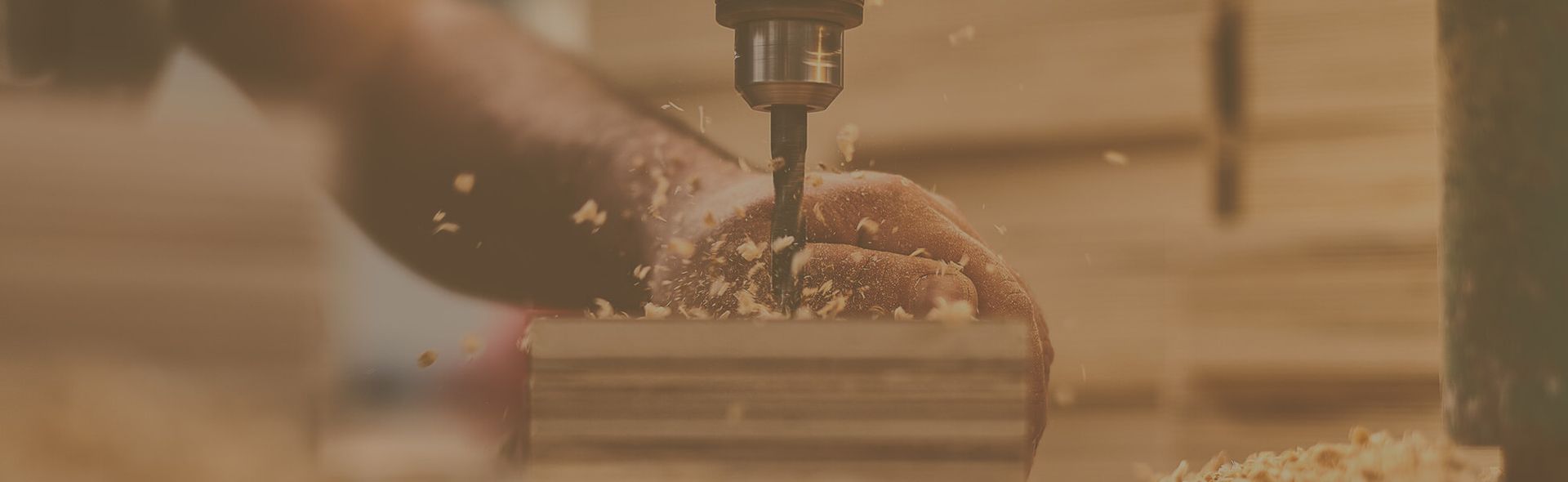 Ein Mann bohrt mit einer Standbohrmaschine in ein Stück Holz
